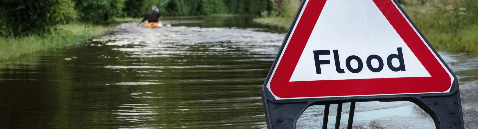 Triangle flood warning sign in foreground of flooded road